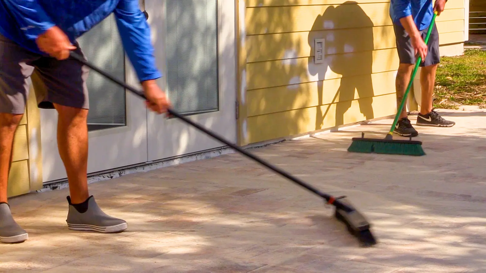Two Sunshine crew members sweeping sand into the joints of a paver patio.